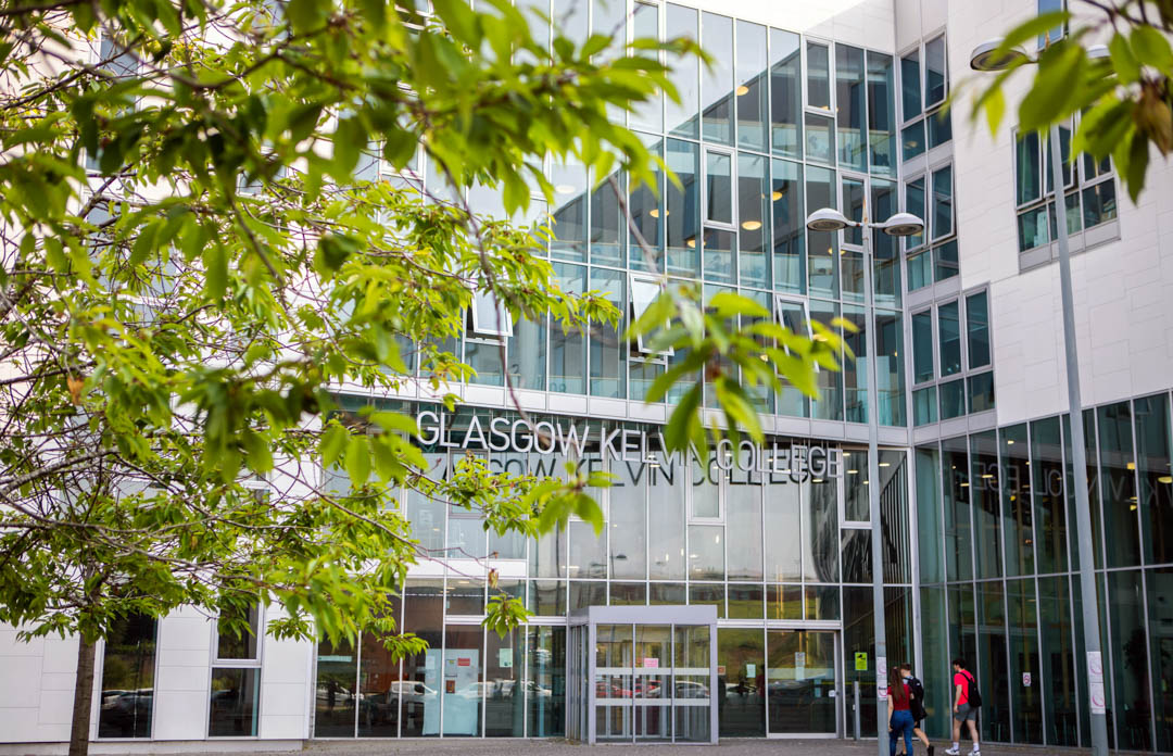 View of Glasgow Kelvin College Springburn Campus entrance seen through leafy trees, showcasing the building’s modern exterior.
