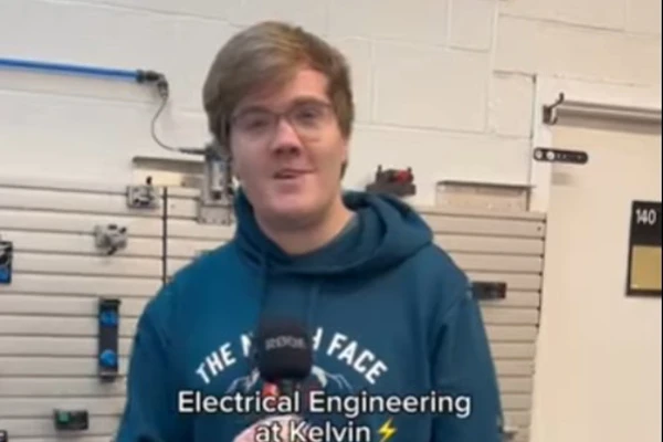 A student in a blue hoodie holding a microphone, standing in front of an electrical engineering workstation at Glasgow Kelvin College. The text overlay reads 'Electrical Engineering at Kelvin ⚡' with the student introducing themselves as Shedon A student in a blue hoodie holding a microphone, standing in front of an electrical engineering workstation at Glasgow Kelvin College. The text overlay reads 'Electrical Engineering at Kelvin ⚡' with the student introducing themselves as Shedon