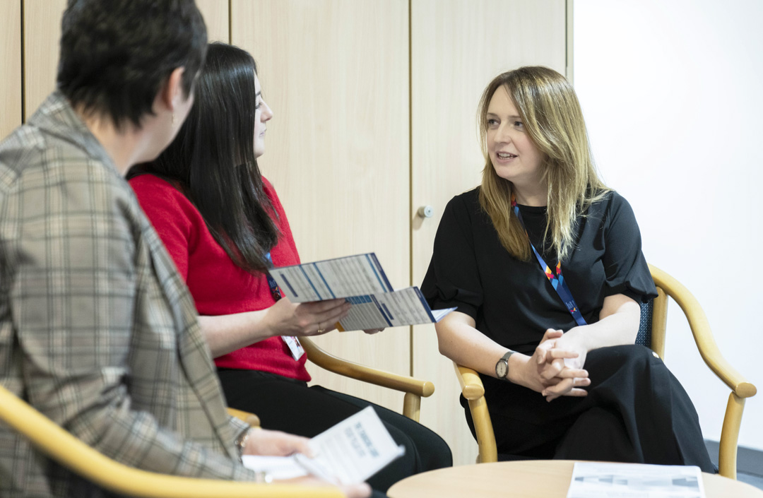 Three Glasgow Kelvin College staff members sitting in discussion, holding leaflets during an informal team meeting