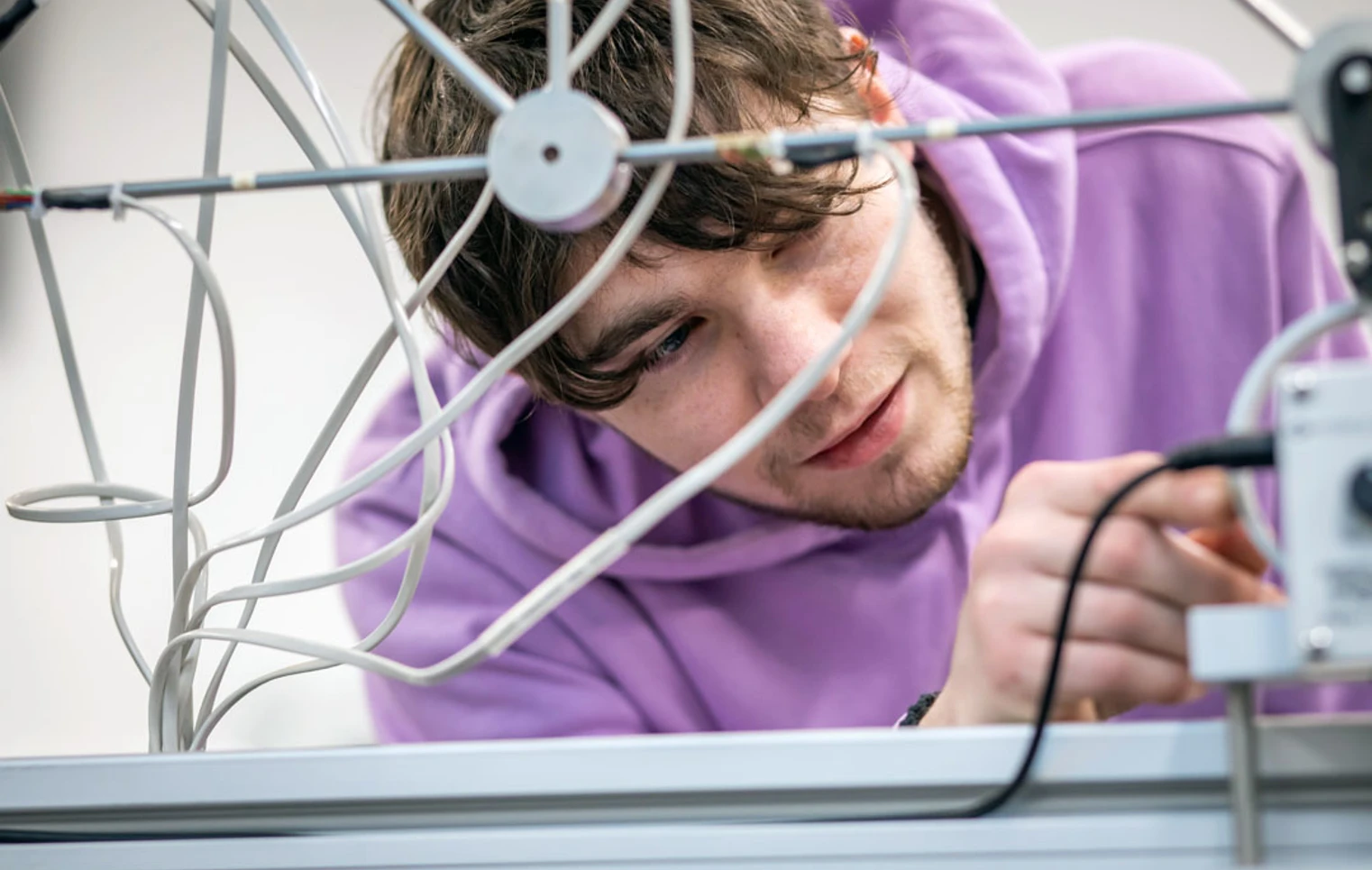 A student in a purple hoodie carefully adjusting wires on a mechanical assembly, focused on a hands-on engineering project. A student in a purple hoodie carefully adjusting wires on a mechanical assembly, focused on a hands-on engineering project.
