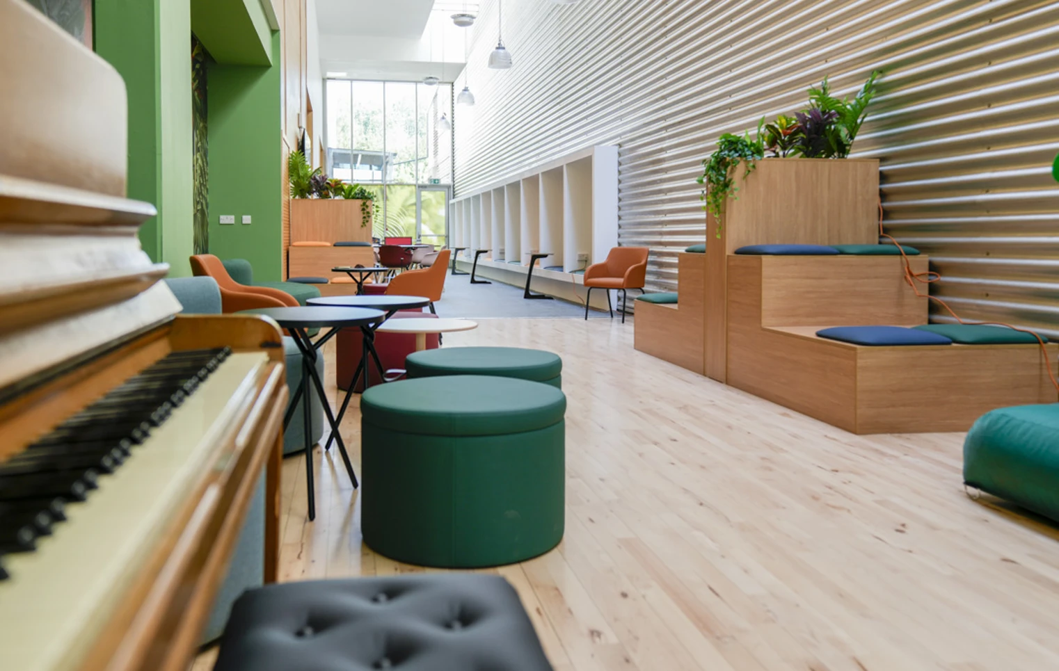 Stylish student lounge with circular stools, lush green sofas, and a mural of tropical plants. Stylish student lounge with circular stools, lush green sofas, and a mural of tropical plants.