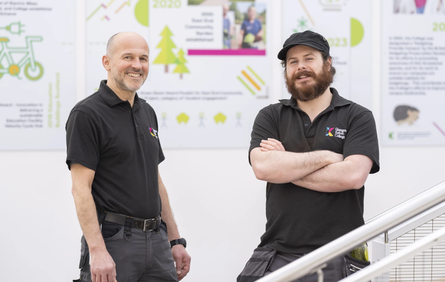 Two male staff members from the Glasgow Kelvin College Estates Team standing indoors, smiling at the camera in front of sustainability-themed posters. Two male staff members from the Glasgow Kelvin College Estates Team standing indoors, smiling at the camera in front of sustainability-themed posters.