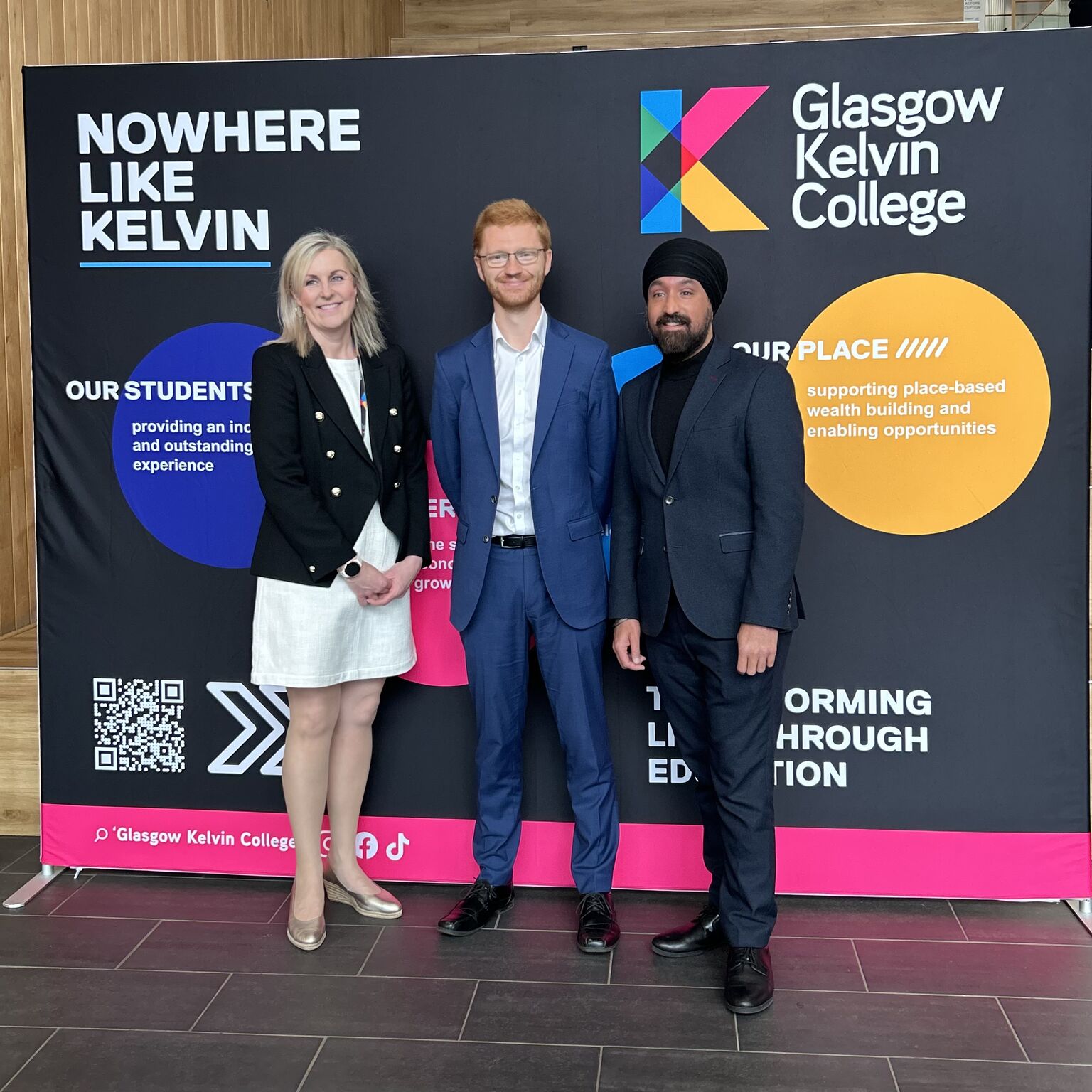 Visitors posing in front of Glasgow Kelvin College branding display during campus visit.
