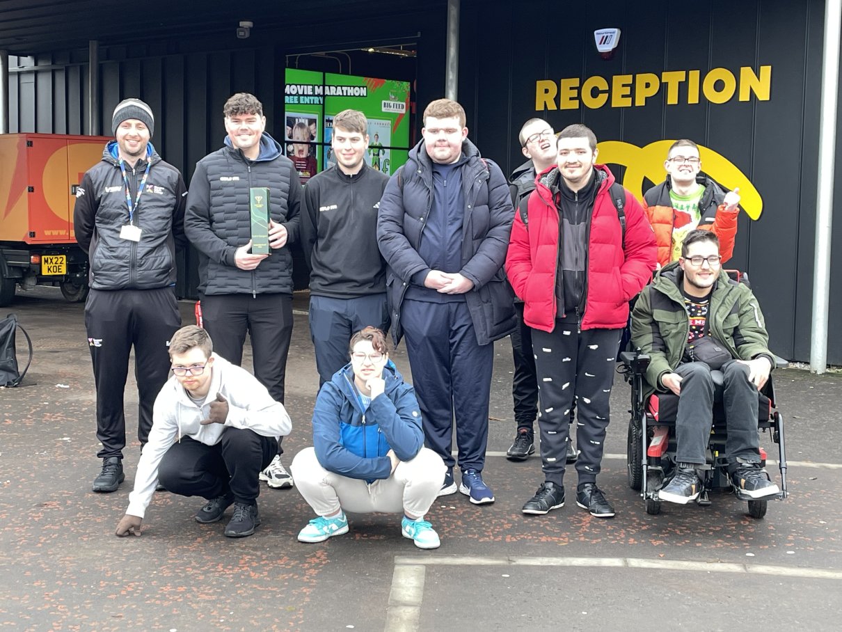 Group of Glasgow Kelvin College students and staff smiling outside the Golf It! reception, some crouching and one in a wheelchair, after a visit.