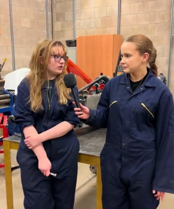 Automotive students in workshop overalls taking part in a filmed interview in a college engineering workshop.