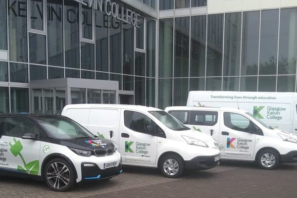 Fleet of electric vehicles branded with Glasgow Kelvin College logos parked outside the college's modern glass-fronted building.