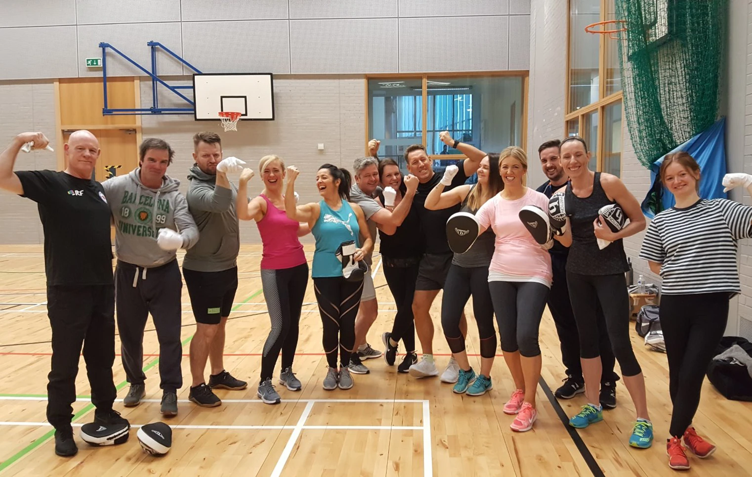Group of Glasgow Kelvin College staff and students smiling and flexing after a fitness session in the gym hall, wearing boxing gloves and pads. Group of Glasgow Kelvin College staff and students smiling and flexing after a fitness session in the gym hall, wearing boxing gloves and pads.