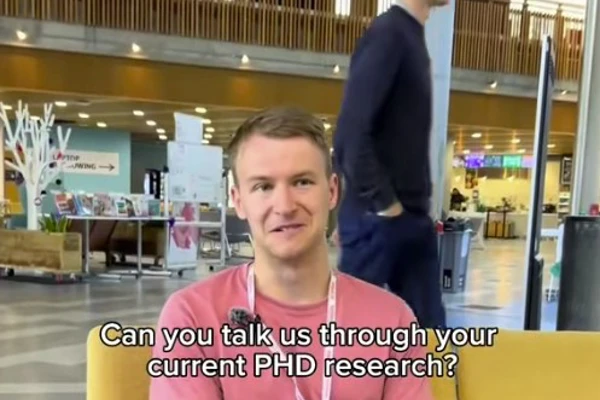 Glen Watt, former Glasgow Kelvin College Science student, sits in the college atrium discussing his PhD research, wearing a pink T-shirt and lanyard. Glen Watt, former Glasgow Kelvin College Science student, sits in the college atrium discussing his PhD research, wearing a pink T-shirt and lanyard.