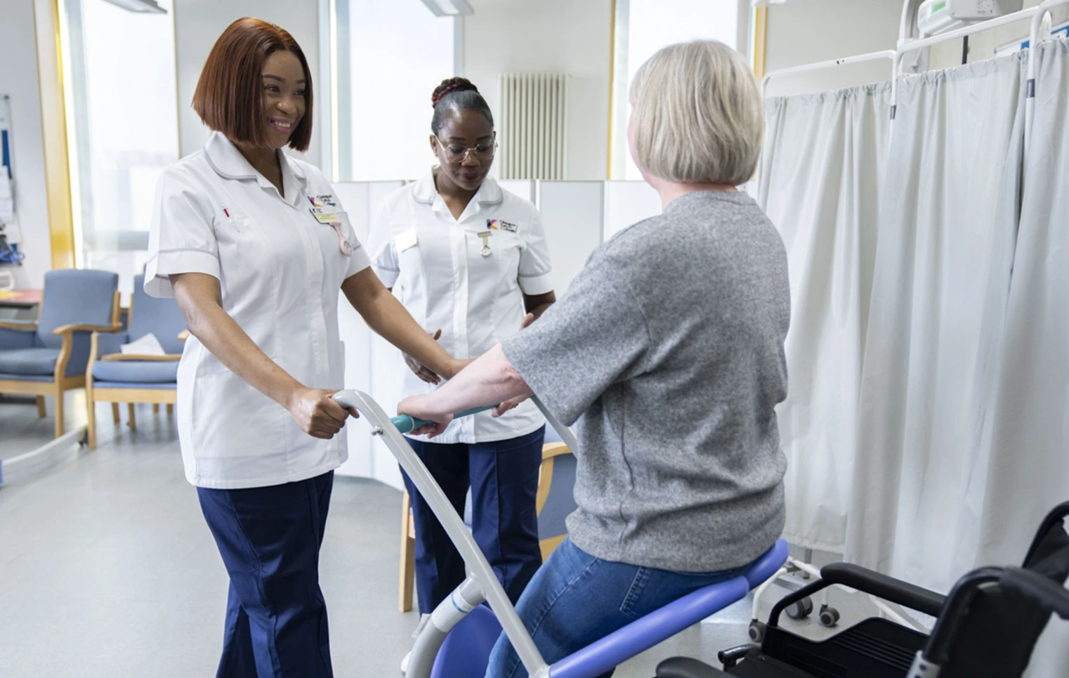 Two healthcare students assist a patient using a mobility aid in a simulated care environment. Two healthcare students assist a patient using a mobility aid in a simulated care environment.