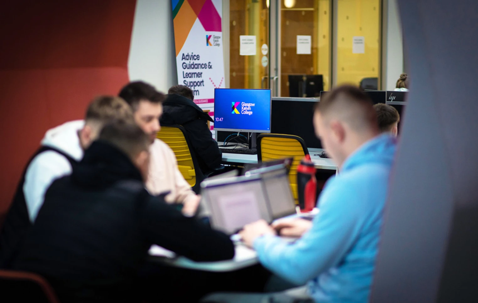 Students working together on laptops in a pod area at Glasgow Kelvin College, with a support services banner and desktop monitors in the background. Students working together on laptops in a pod area at Glasgow Kelvin College, with a support services banner and desktop monitors in the background.