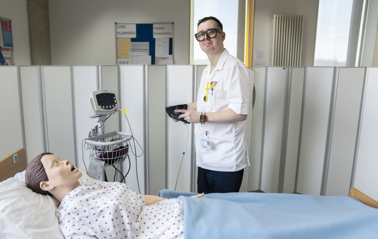 Student prepares to check vital signs on a training mannequin in a simulated hospital ward. Student prepares to check vital signs on a training mannequin in a simulated hospital ward.