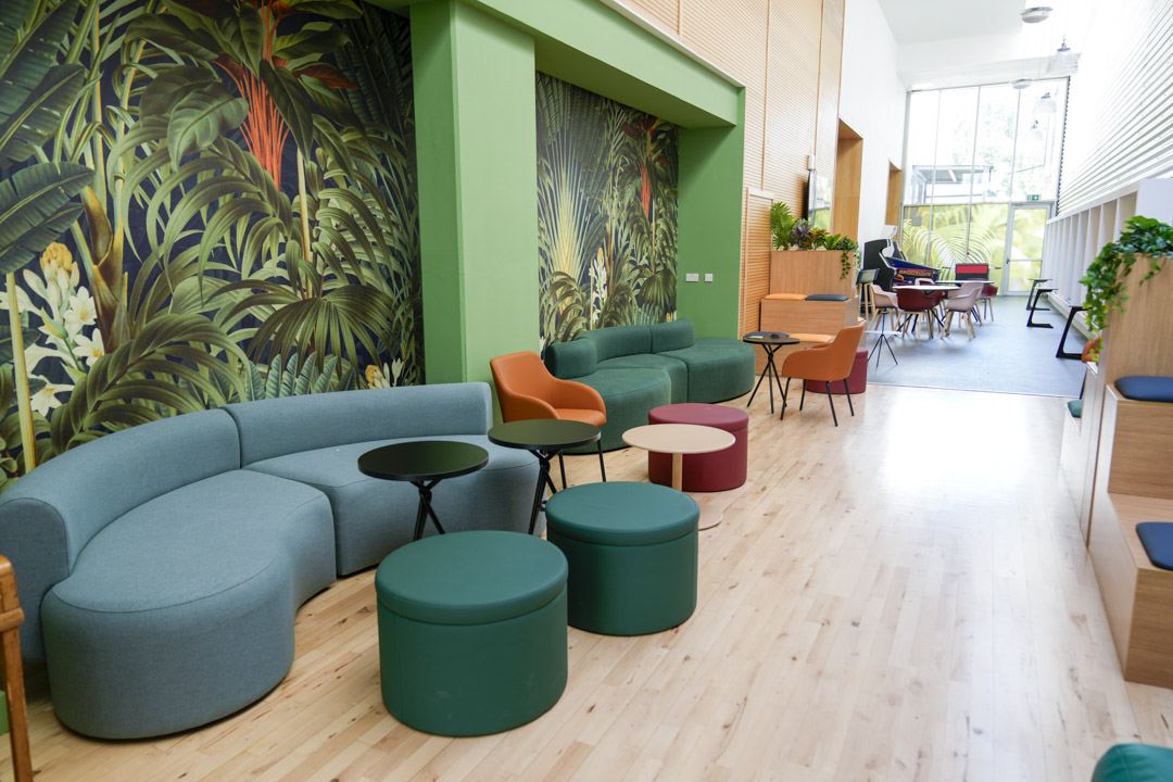 Seating area with green and orange cushioned benches, black side tables, and colourful wallpaper in a student hub.