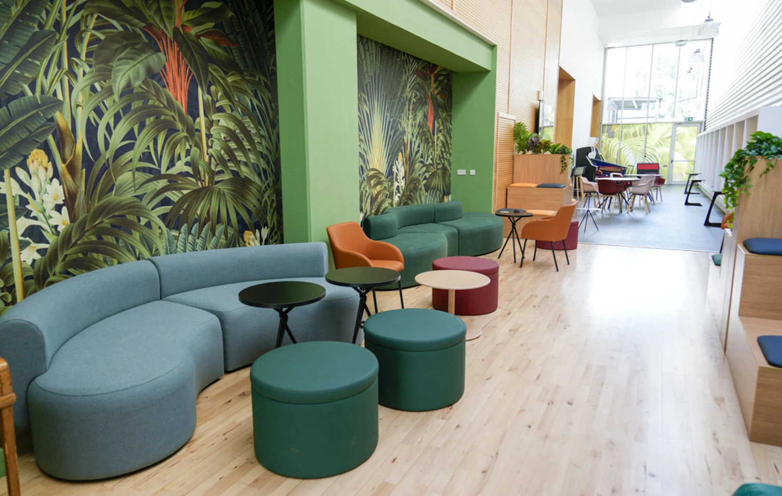 Seating area with green and orange cushioned benches, black side tables, and colourful wallpaper in a student hub. Seating area with green and orange cushioned benches, black side tables, and colourful wallpaper in a student hub.