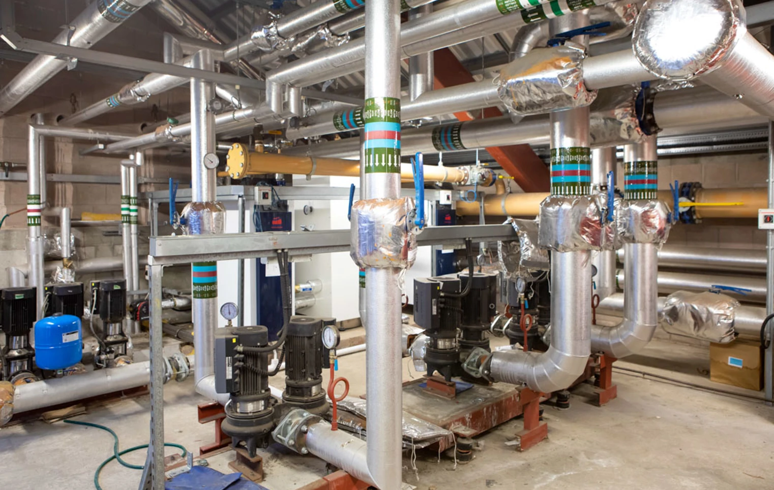 A network of insulated industrial pipes, pumps, and control valves in a large building services training facility A network of insulated industrial pipes, pumps, and control valves in a large building services training facility