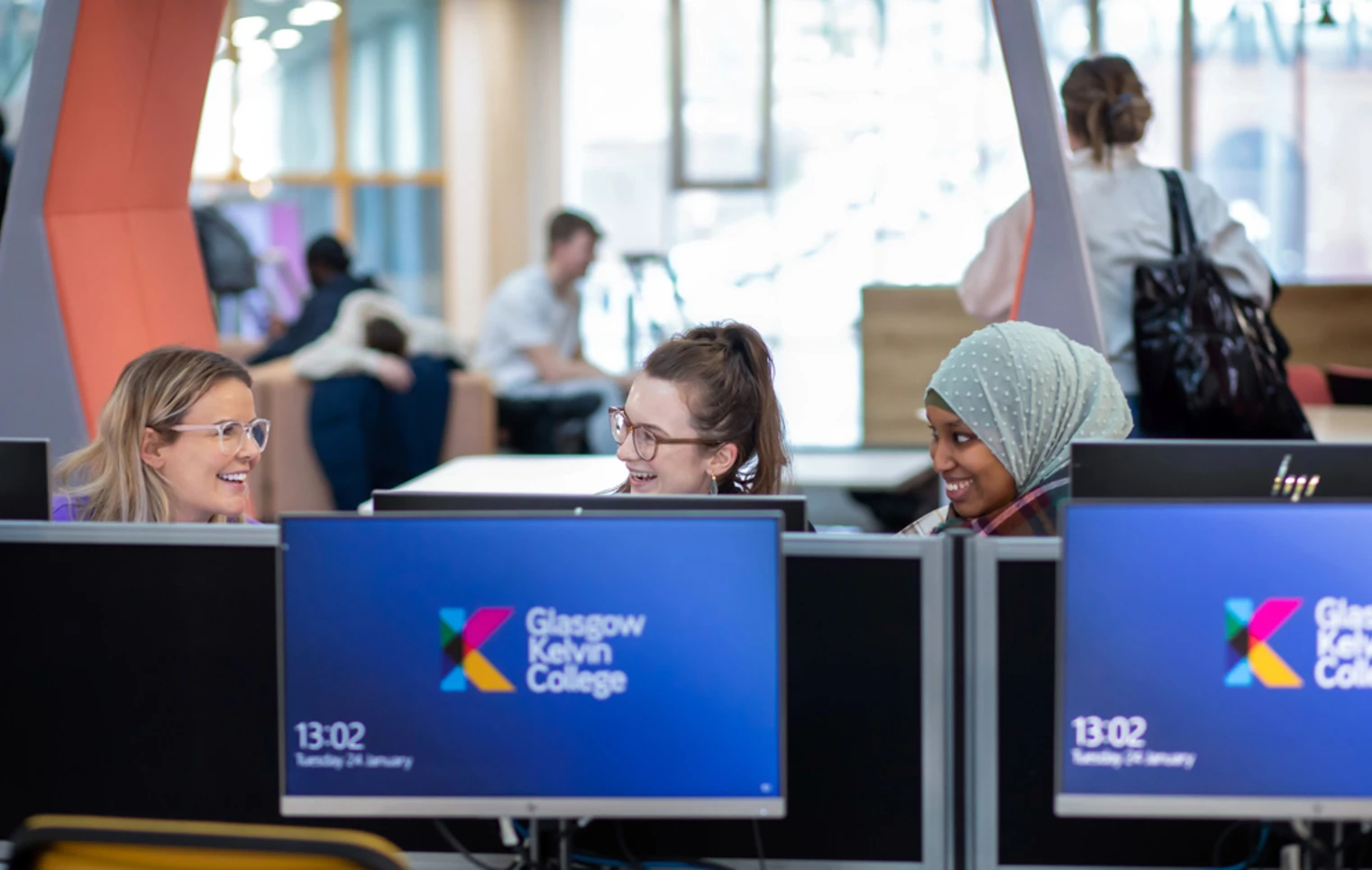 Three female students smiling and chatting while using desktop computers in the library area at Glasgow Kelvin College’s Springburn Campus. Three female students smiling and chatting while using desktop computers in the library area at Glasgow Kelvin College’s Springburn Campus.