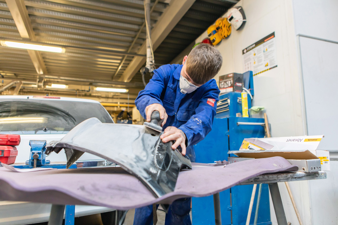 Student in blue overalls sanding a car panel in the Glasgow Kelvin College automotive workshop.