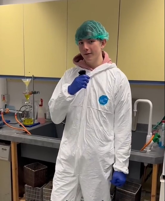 Science student Robert wearing protective clothing and speaking into a microphone in a college laboratory.