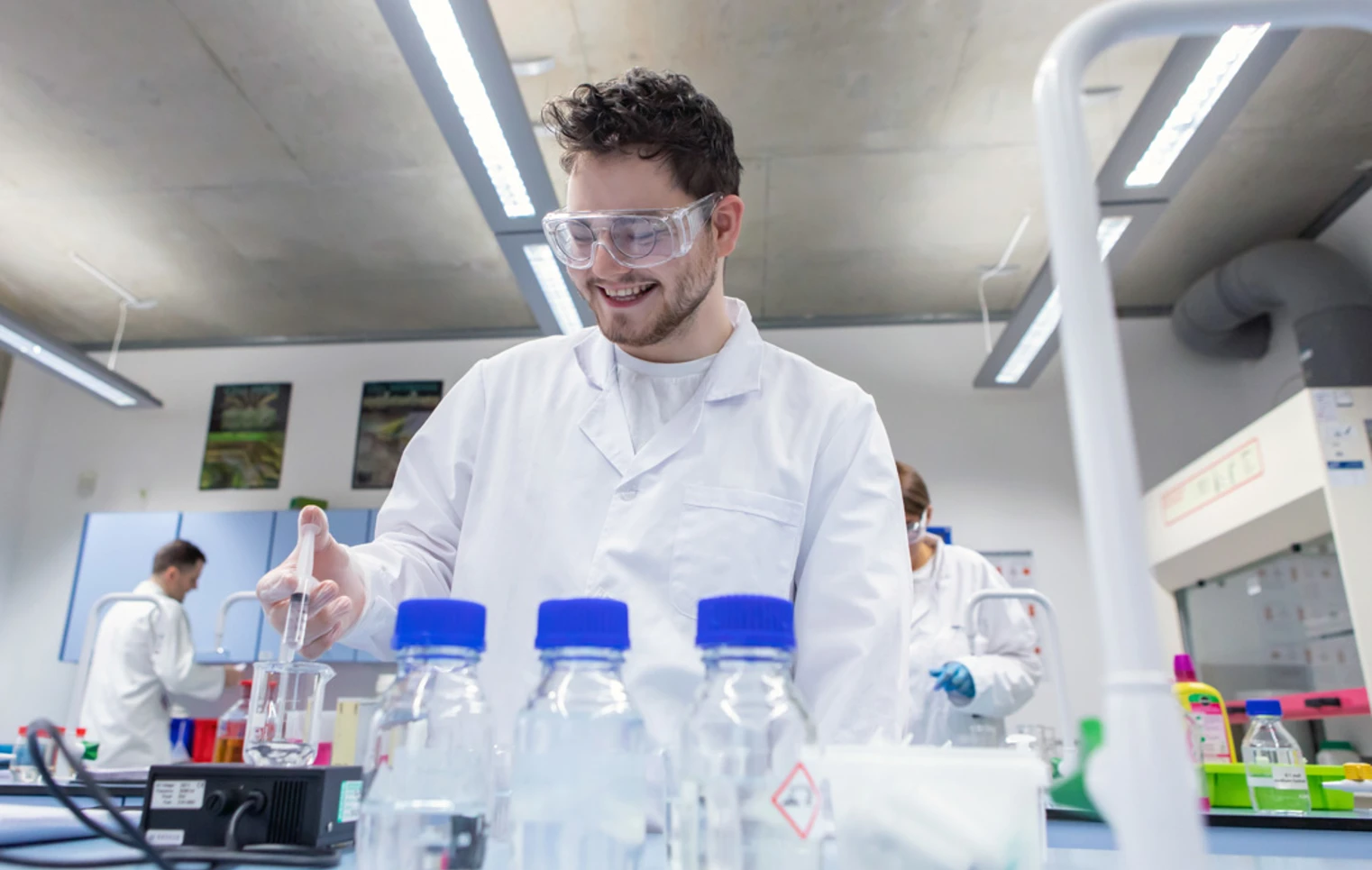 Male student wearing lab coat and goggles pipetting liquid during science experiment Male student wearing lab coat and goggles pipetting liquid during science experiment