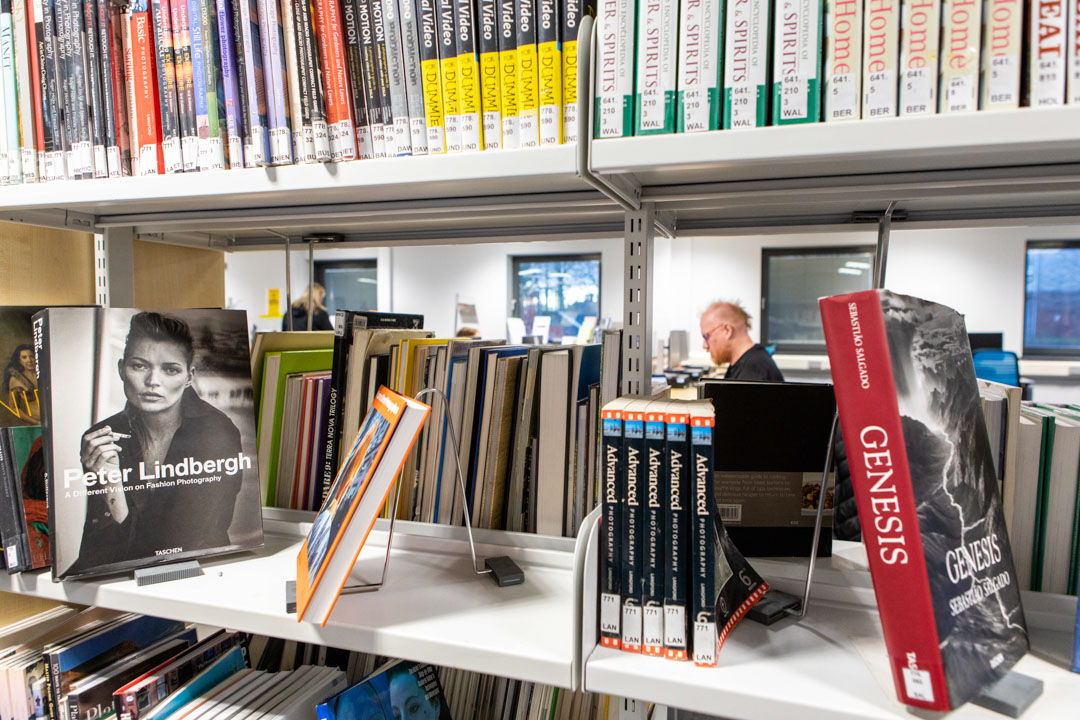Books on display in the Easterhouse Campus library at Glasgow Kelvin College, with a student working in the background.