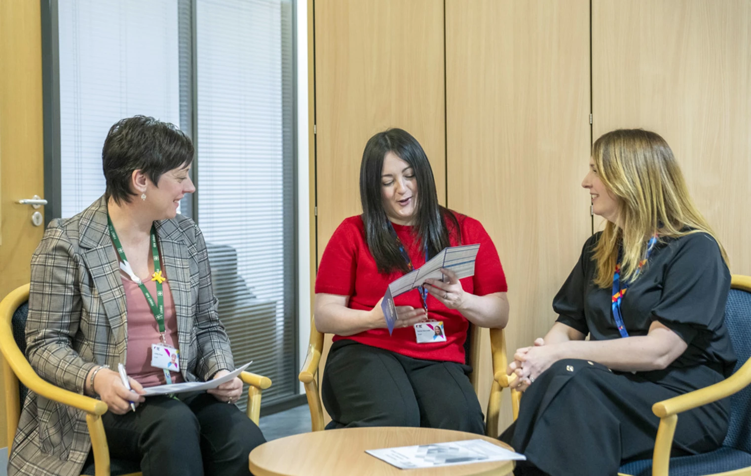 Three Glasgow Kelvin College staff members sitting together in discussion, with one holding a leaflet, in an office setting. Three Glasgow Kelvin College staff members sitting together in discussion, with one holding a leaflet, in an office setting.