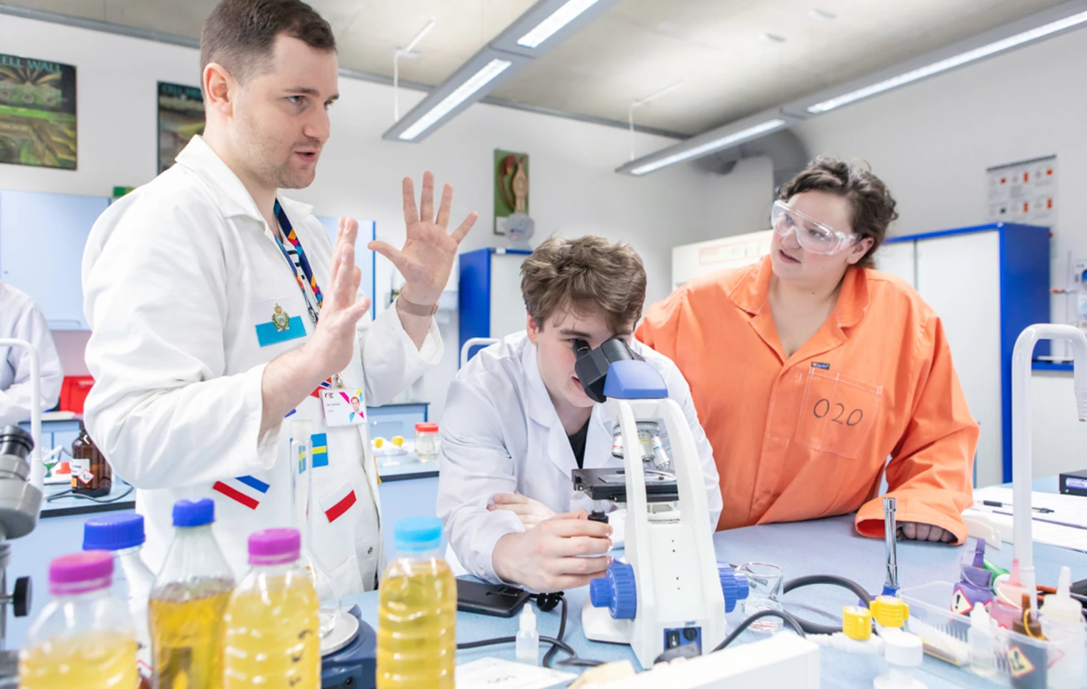 Science lecturer guiding a student on microscope use with classmates observing in the lab at Glasgow Kelvin College Science lecturer guiding a student on microscope use with classmates observing in the lab at Glasgow Kelvin College