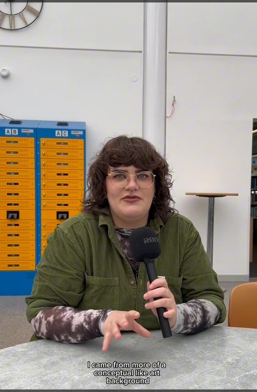 Digital Design student Georgia speaking on camera about her experience at Glasgow Kelvin College, seated at a table with lockers in the background.