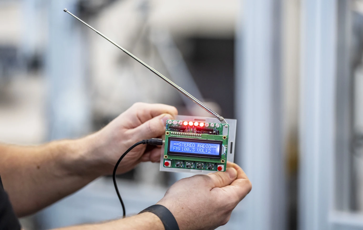 Close-up of a small electronic device with an LCD screen displaying radio frequency settings, held by a person in a technical lab. Close-up of a small electronic device with an LCD screen displaying radio frequency settings, held by a person in a technical lab.