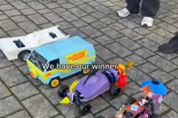 A group of people standing around three colorful, custom-built model cars at the finish line of the Annual Kelvin CAD Car Race. The winning car, a bright blue and yellow van, is in the foreground with a "Winner" sticker, while the other two cars, one purple and one red, are beside it on a paved surface. A group of people standing around three colorful, custom-built model cars at the finish line of the Annual Kelvin CAD Car Race. The winning car, a bright blue and yellow van, is in the foreground with a "Winner" sticker, while the other two cars, one purple and one red, are beside it on a paved surface.