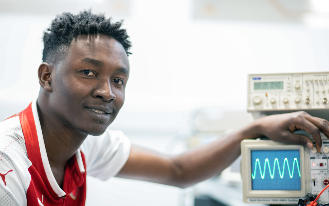 Close-up of a student in a red football jersey adjusting an oscilloscope, displaying a waveform on the screen.